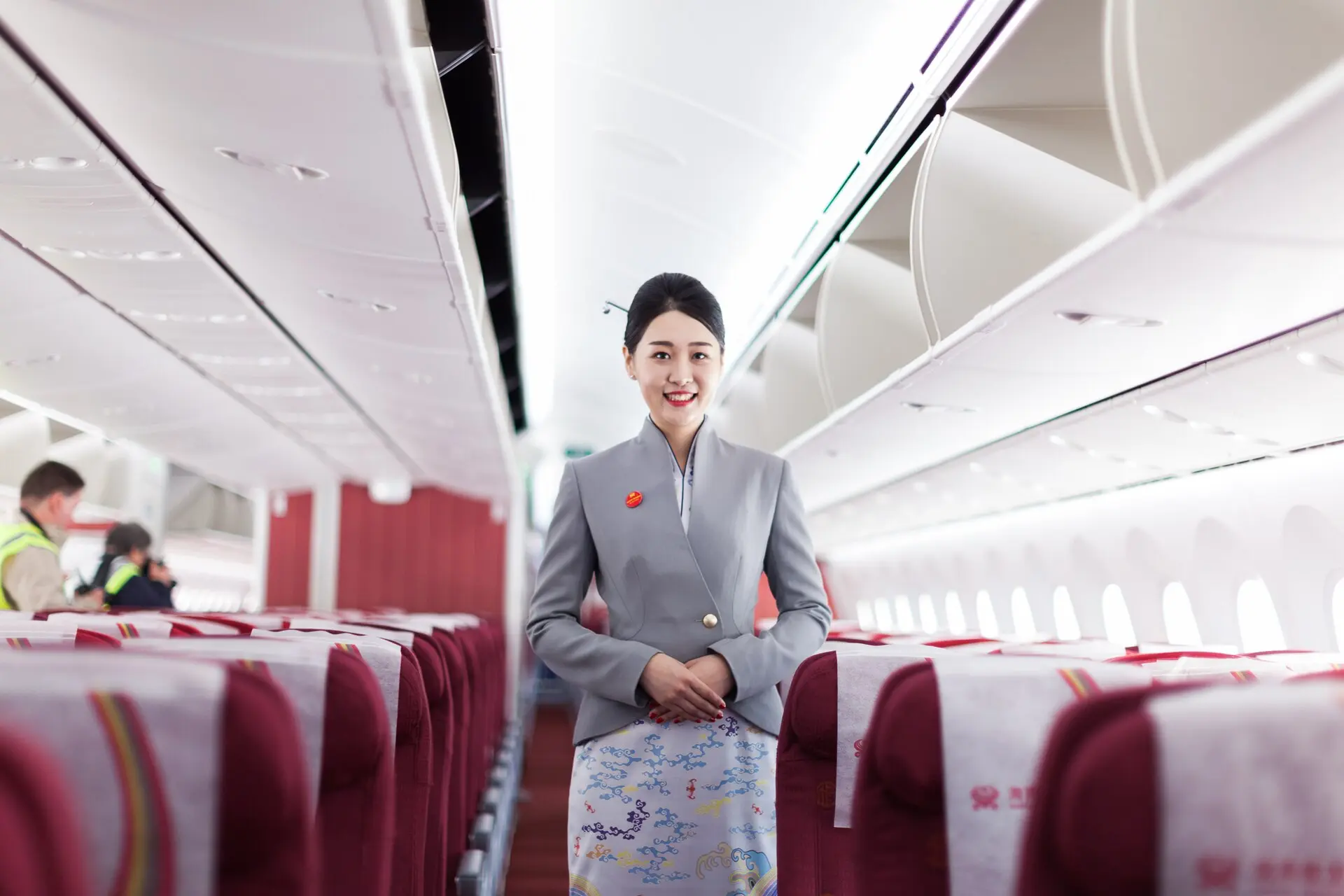 ลูกเรือ Hainan Airlines ในชุดยูนิฟอร์มสีเทา ยืนยิ้มในห้องโดยสาร